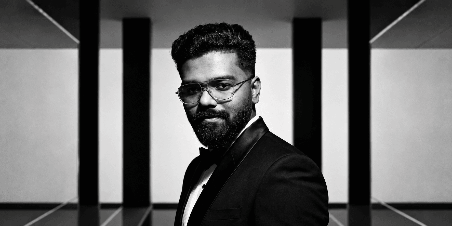 A man in a tuxedo poses confidently against a geometric black and white background