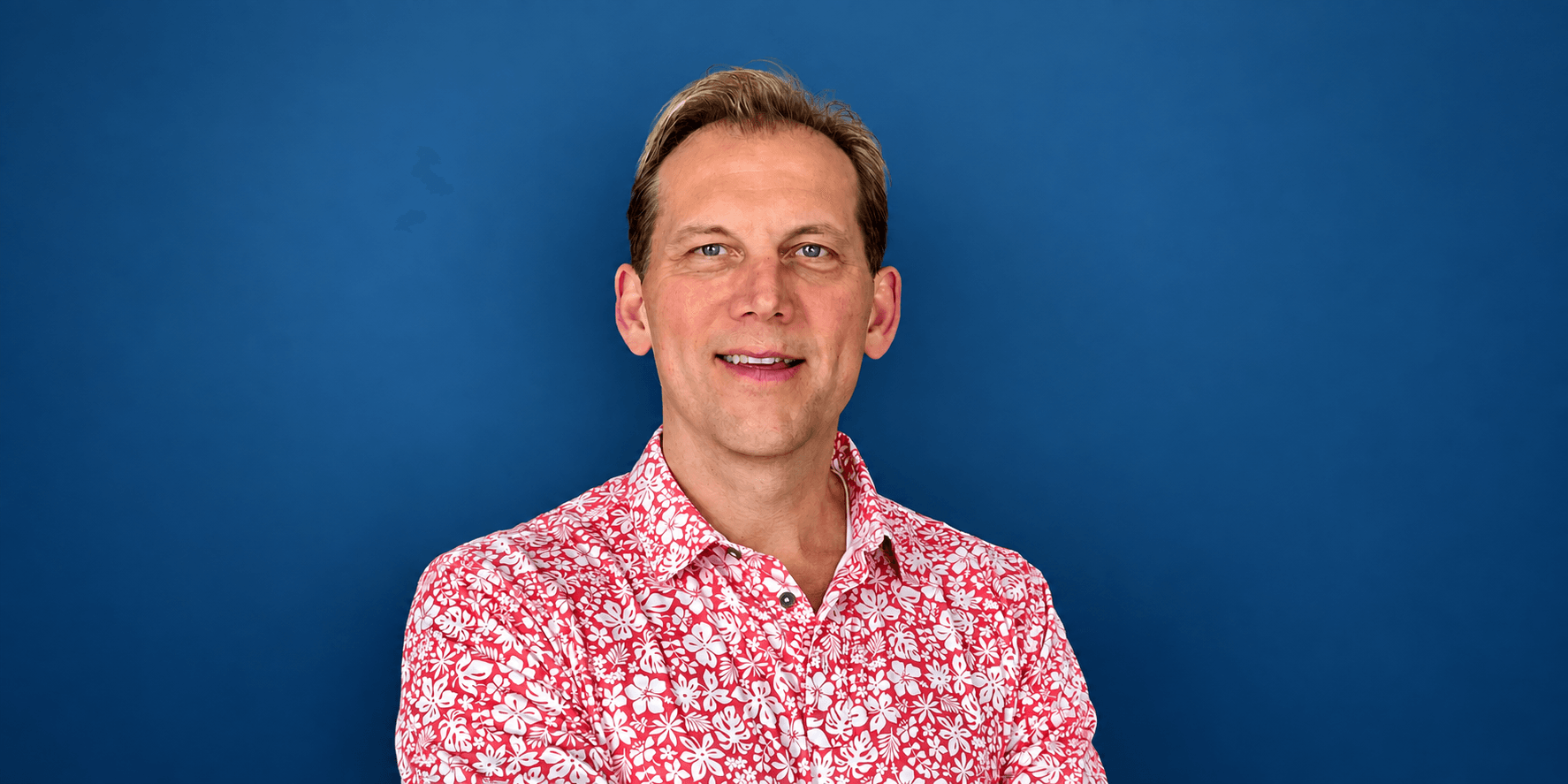 Smiling man in a floral shirt against a blue background