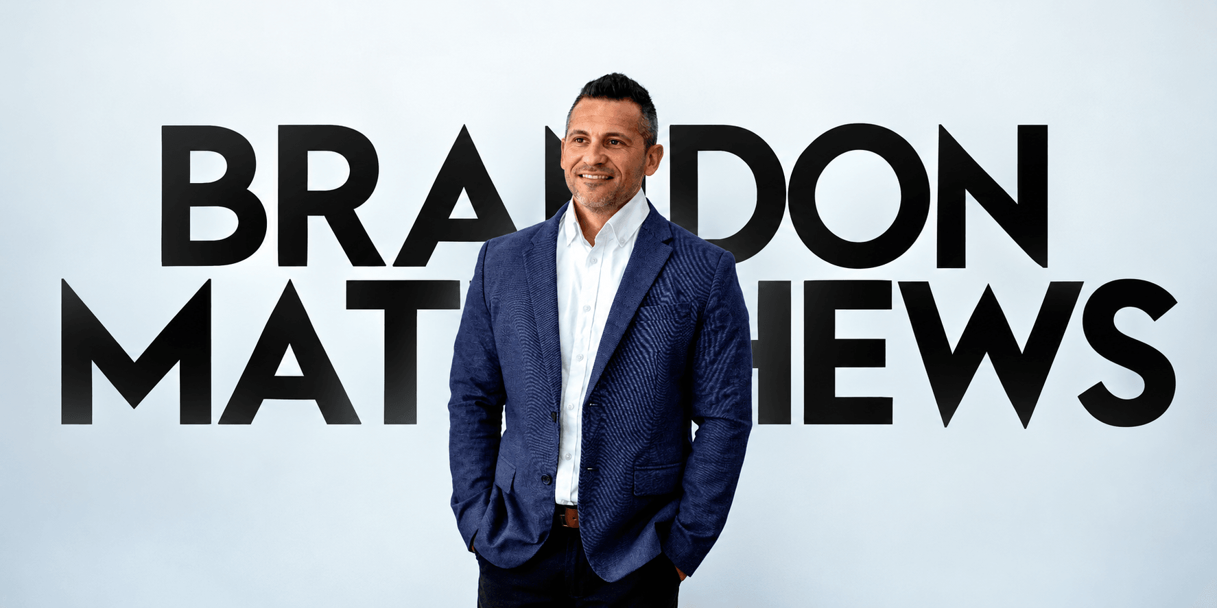 Smiling man in a blazer stands in front of a bold name backdrop