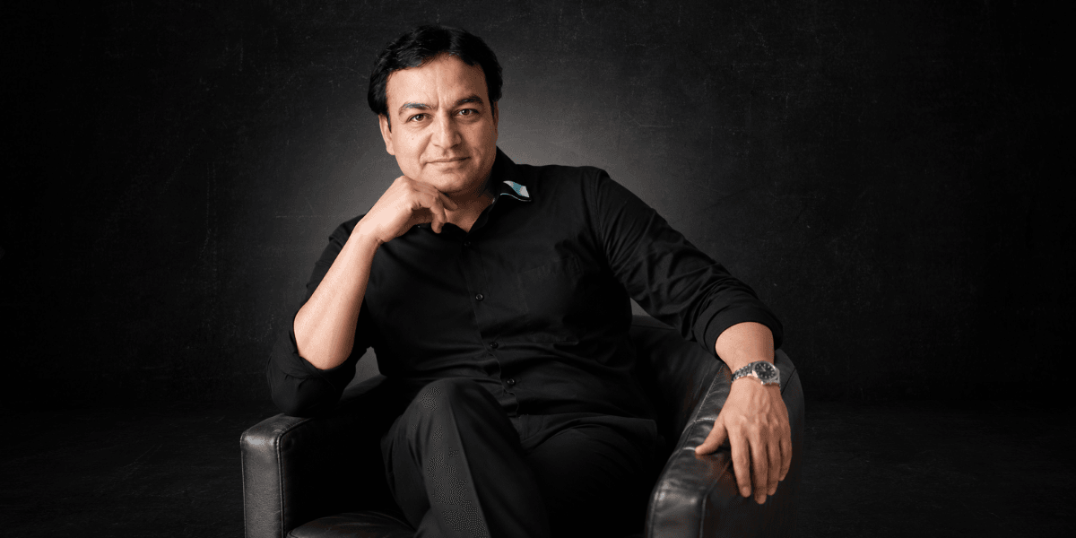 Man in a black shirt seated in a brown armchair against a dark background