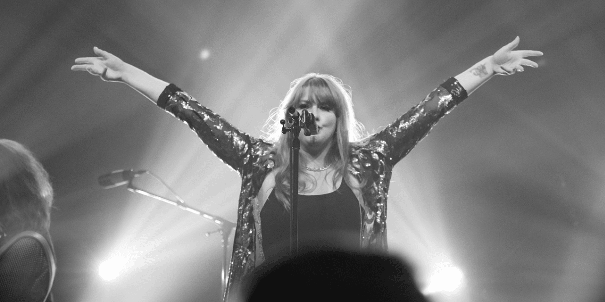 Singer performing on stage with arms raised, wearing a sparkling black outfit