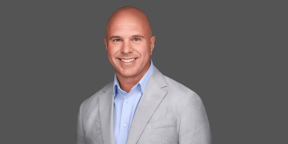A smiling man in a light gray blazer, with a clean background.