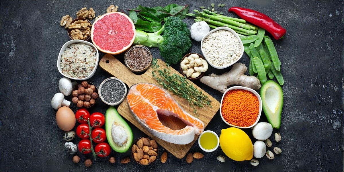 Colorful array of whole foods, including salmon, avocado, vegetables, nuts, and grains, representing a nutrient-dense diet.