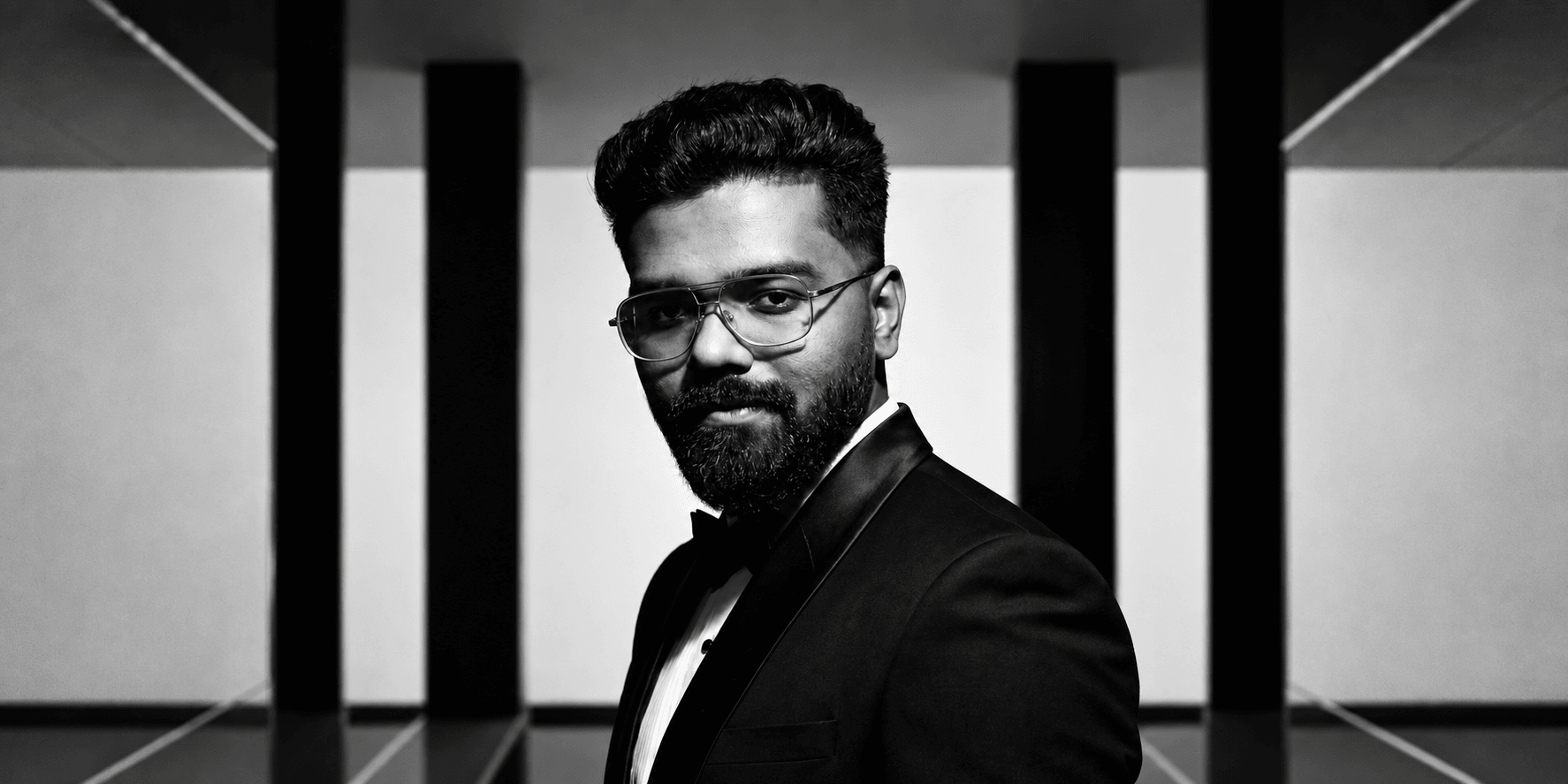 A man in a tuxedo poses confidently against a geometric black and white background