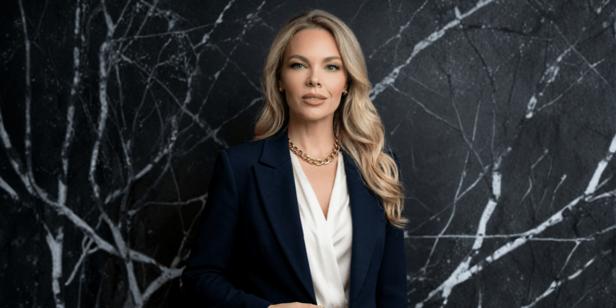 A woman in a blazer stands against a textured dark background with white patterns