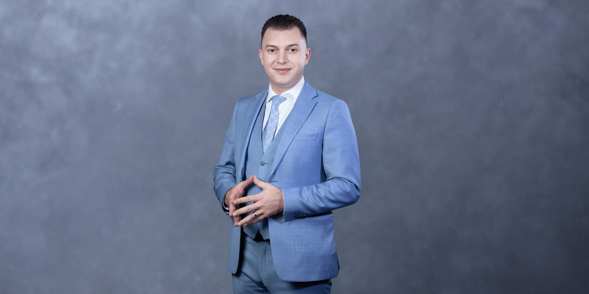 Man in a light blue suit stands confidently against a gray background
