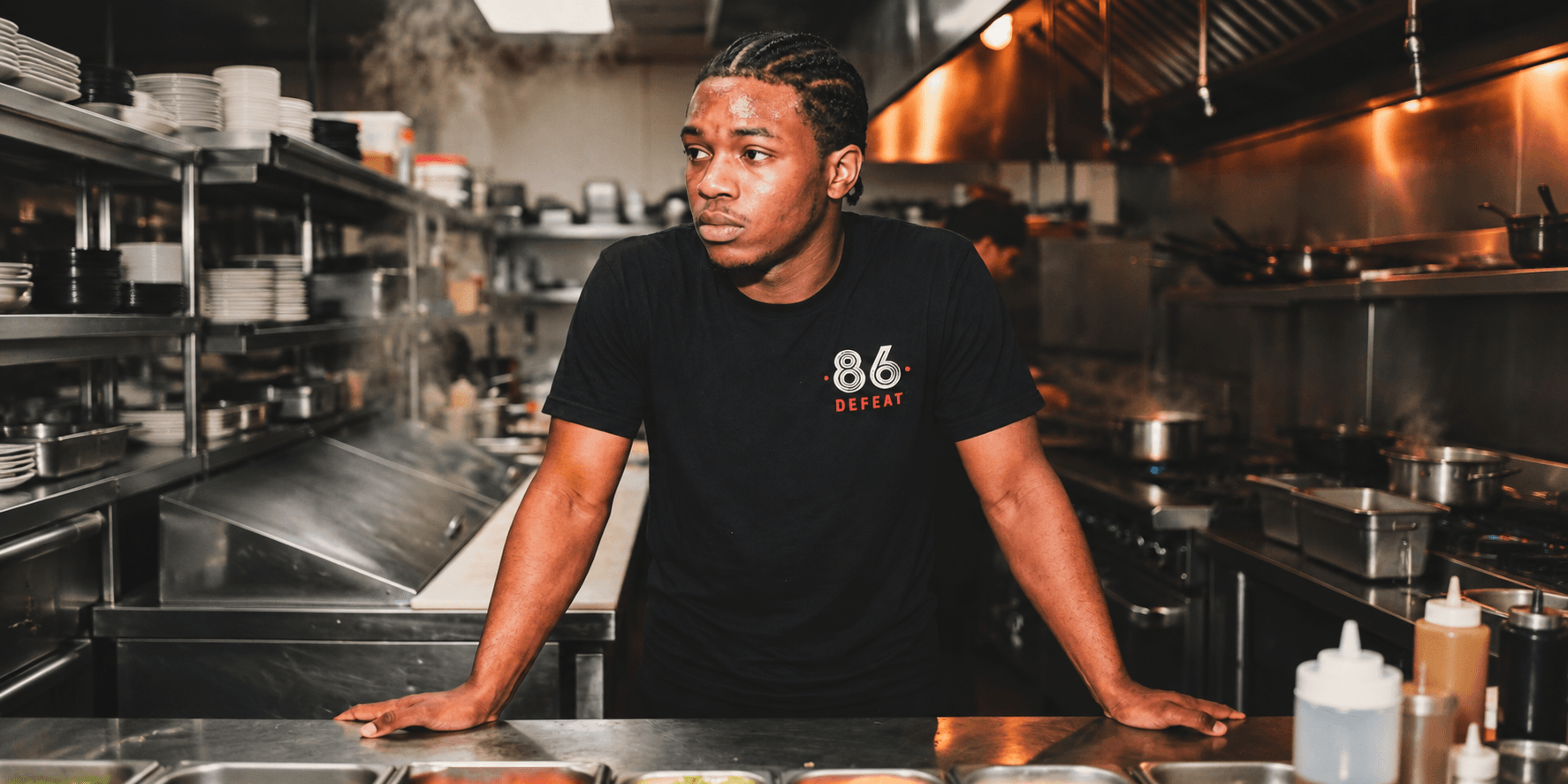 Young man in a black shirt stands in a bustling restaurant kitchen