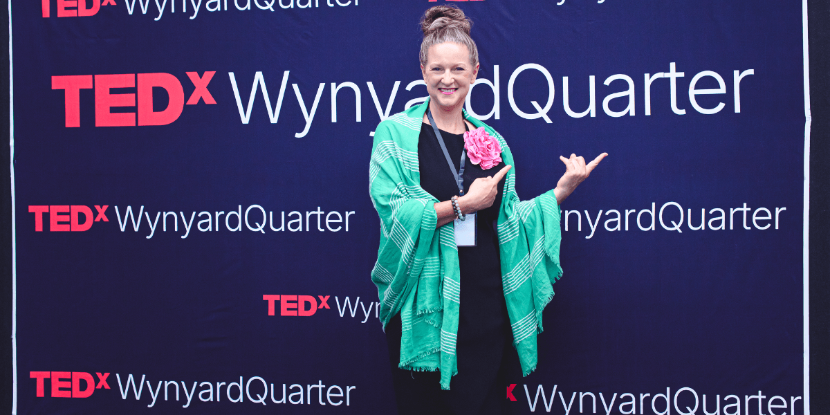 Person in a green shawl posing with a flower at a TEDx event backdrop