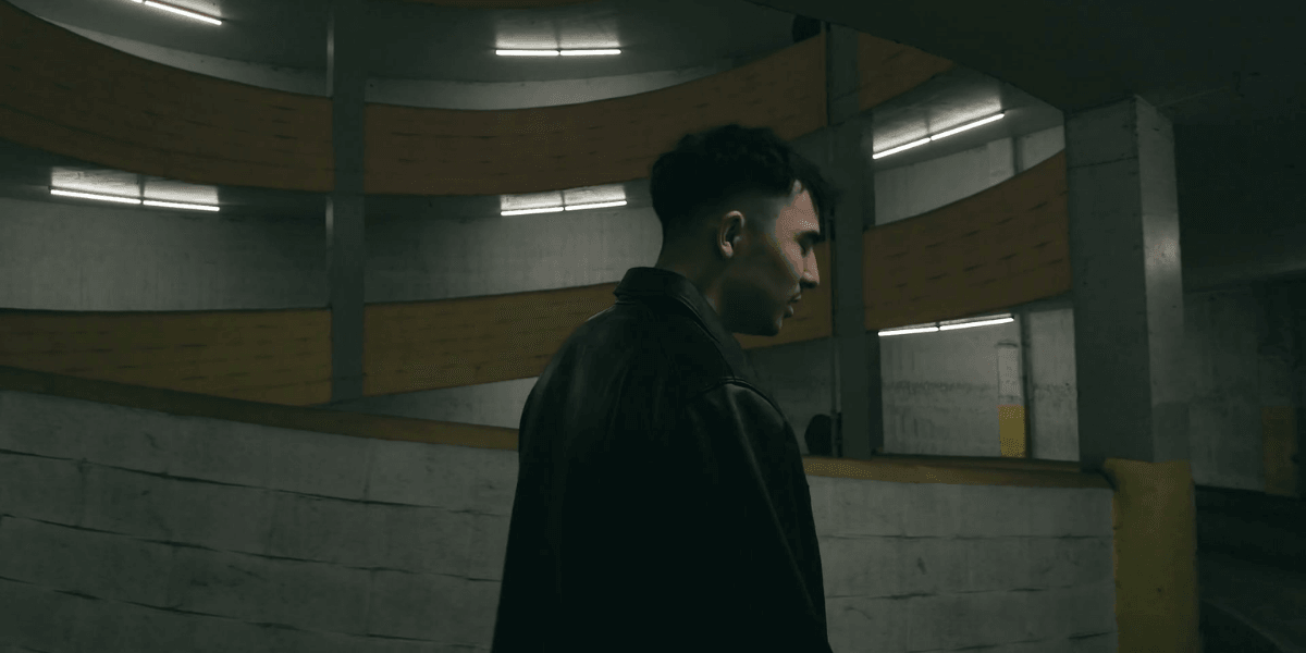 A person in a leather jacket stands in a dimly lit parking garage.