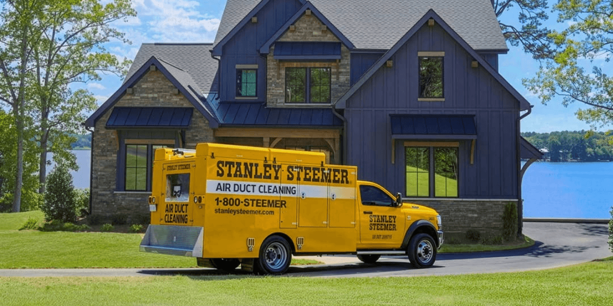 Yellow Stanley Steemer truck parked in front of a modern house by a lake