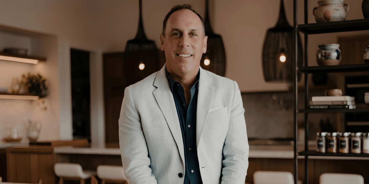 Man in a light suit stands confidently in a modern kitchen setting