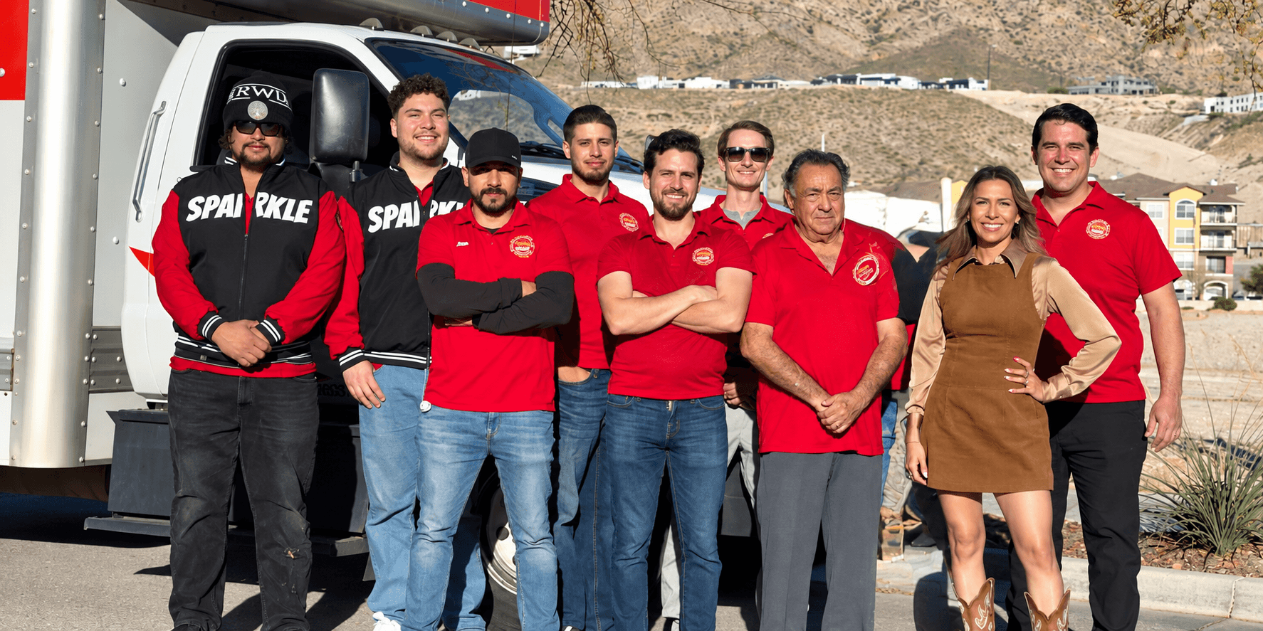 Group of workers in red shirts posing beside a moving truck in a sunny location