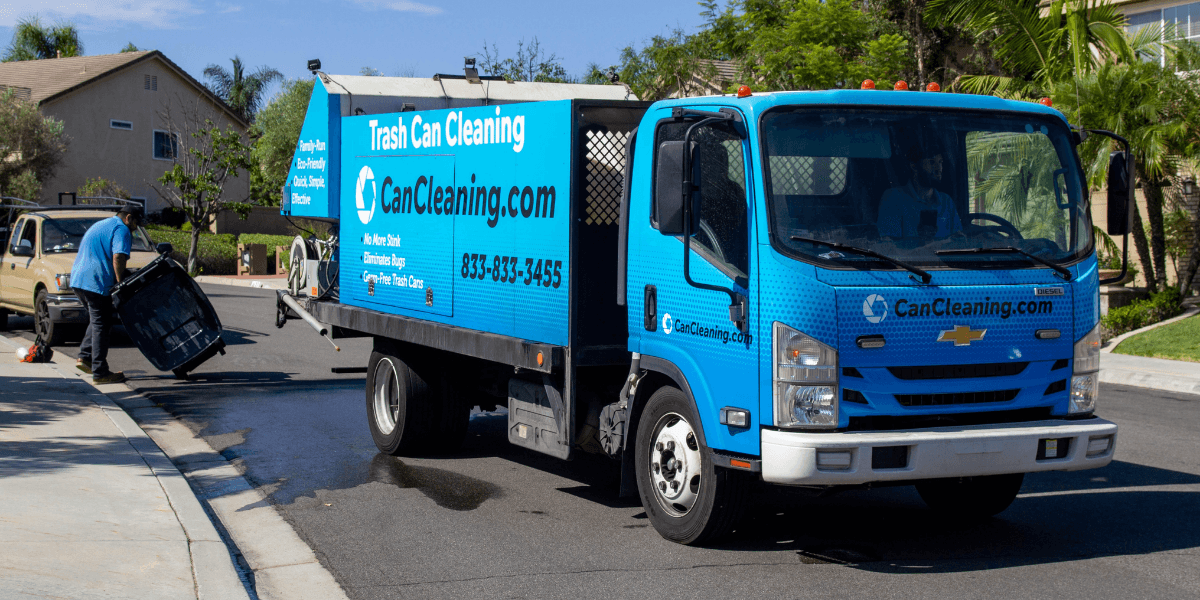 Blue trash cleaning truck parked on a residential street with a worker using equipment