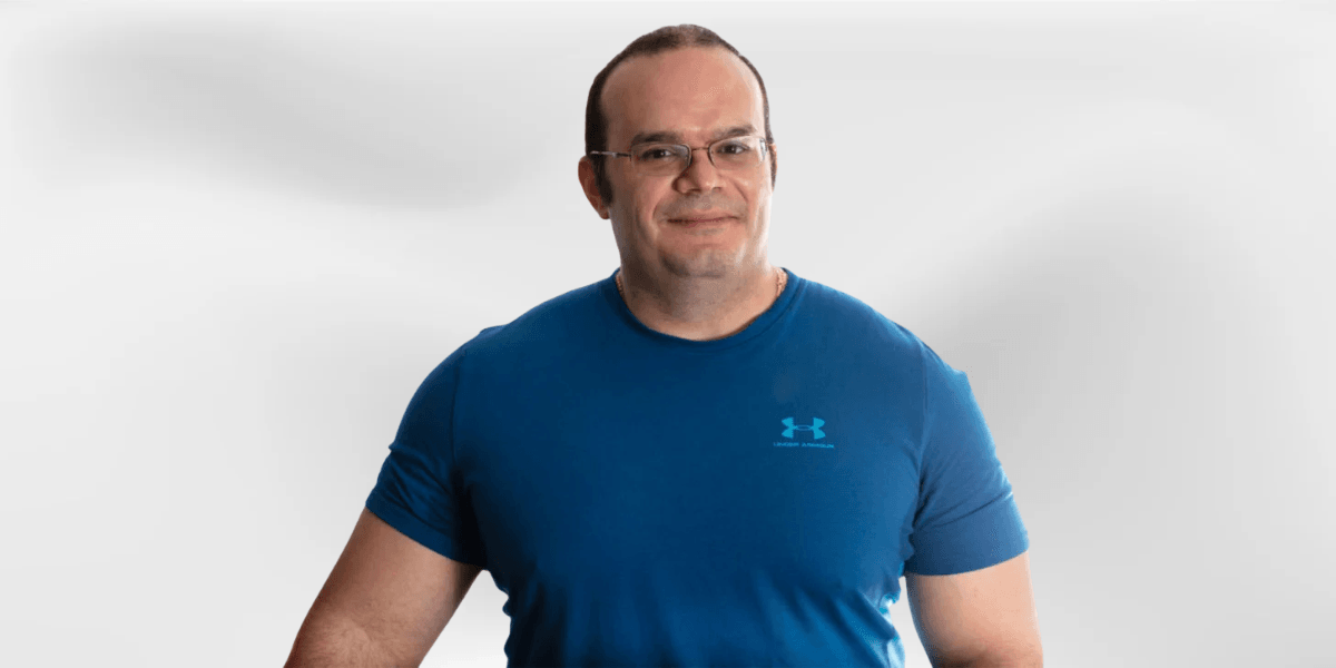 Man in a blue athletic shirt smiling against a light gray background