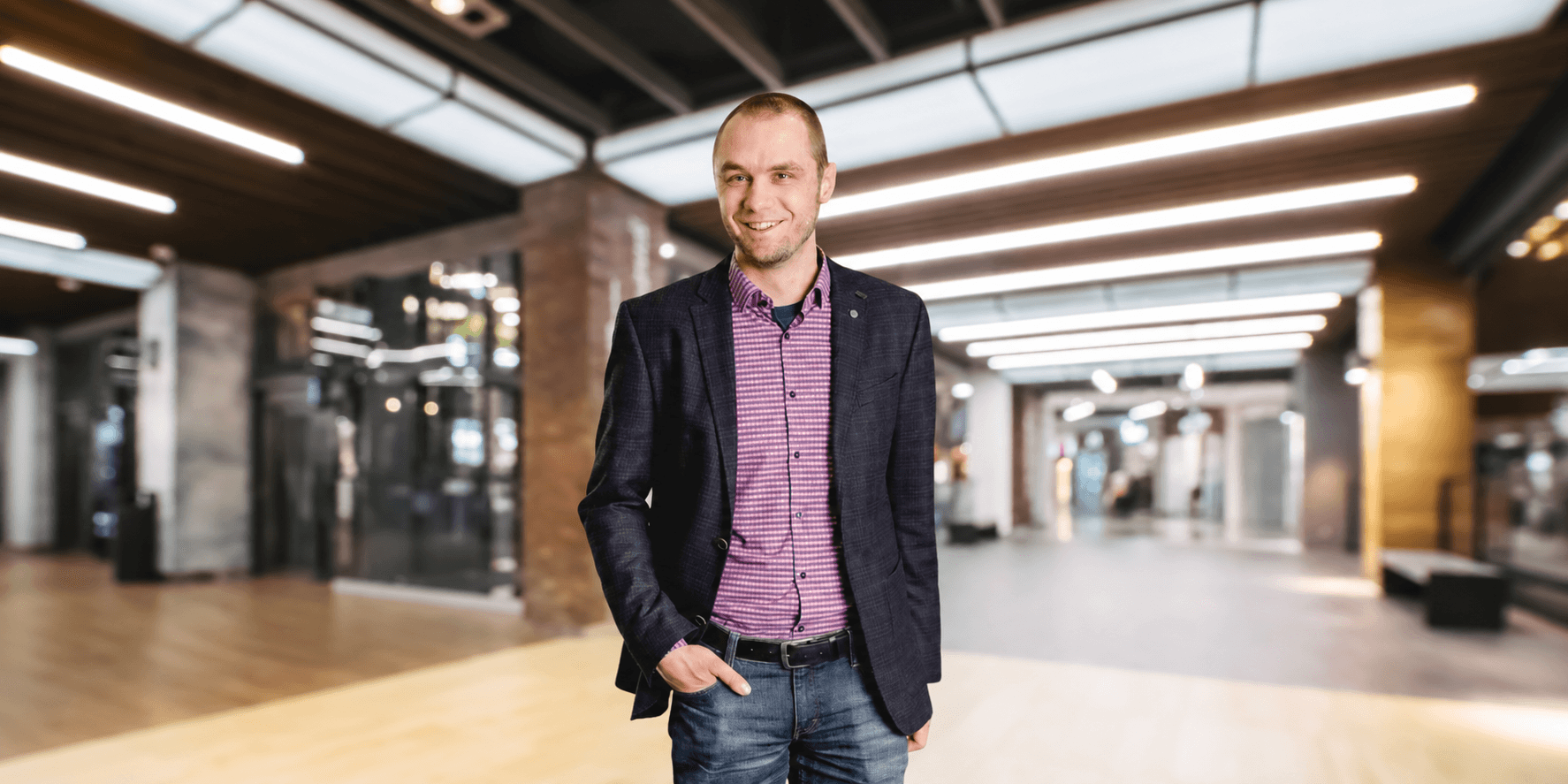 Smiling man in a blazer and striped shirt standing in a modern interior space