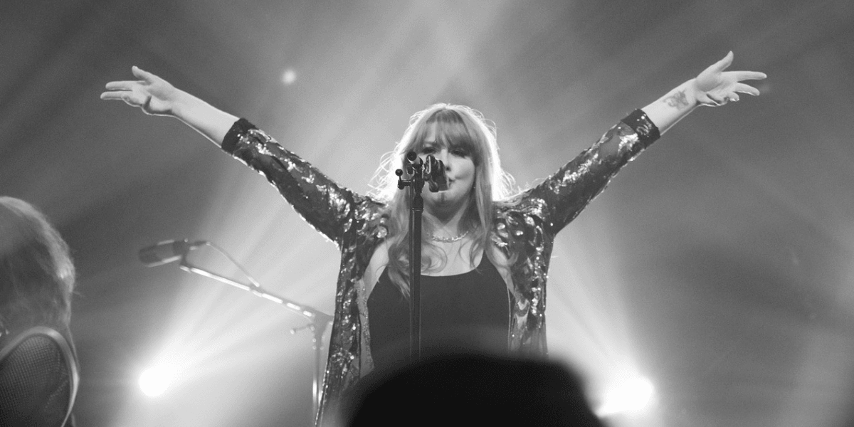 Singer performing on stage with arms raised, wearing a sparkling black outfit