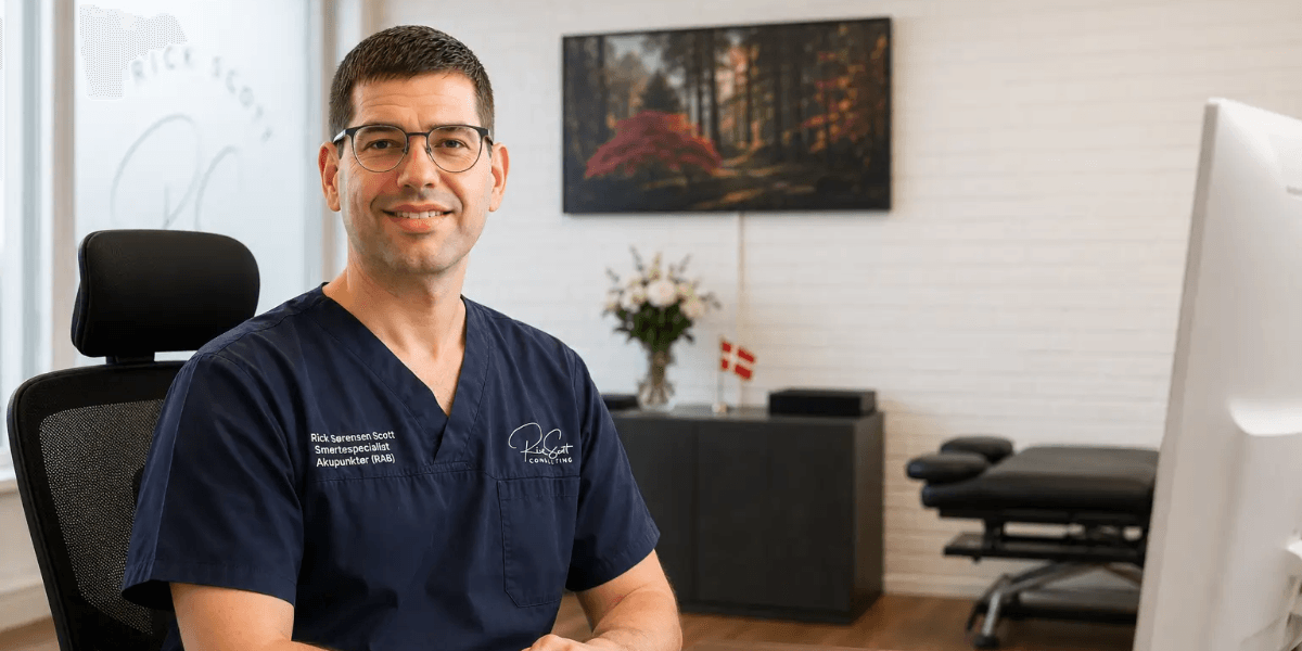 A smiling professional in scrubs sits in a modern office environment.