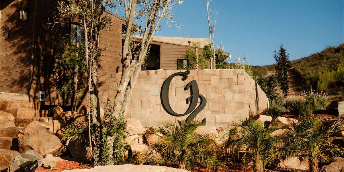 Modern stone wall with O₂ Resort Valle logo, surrounded by lush greenery and palm trees in a tranquil setting.