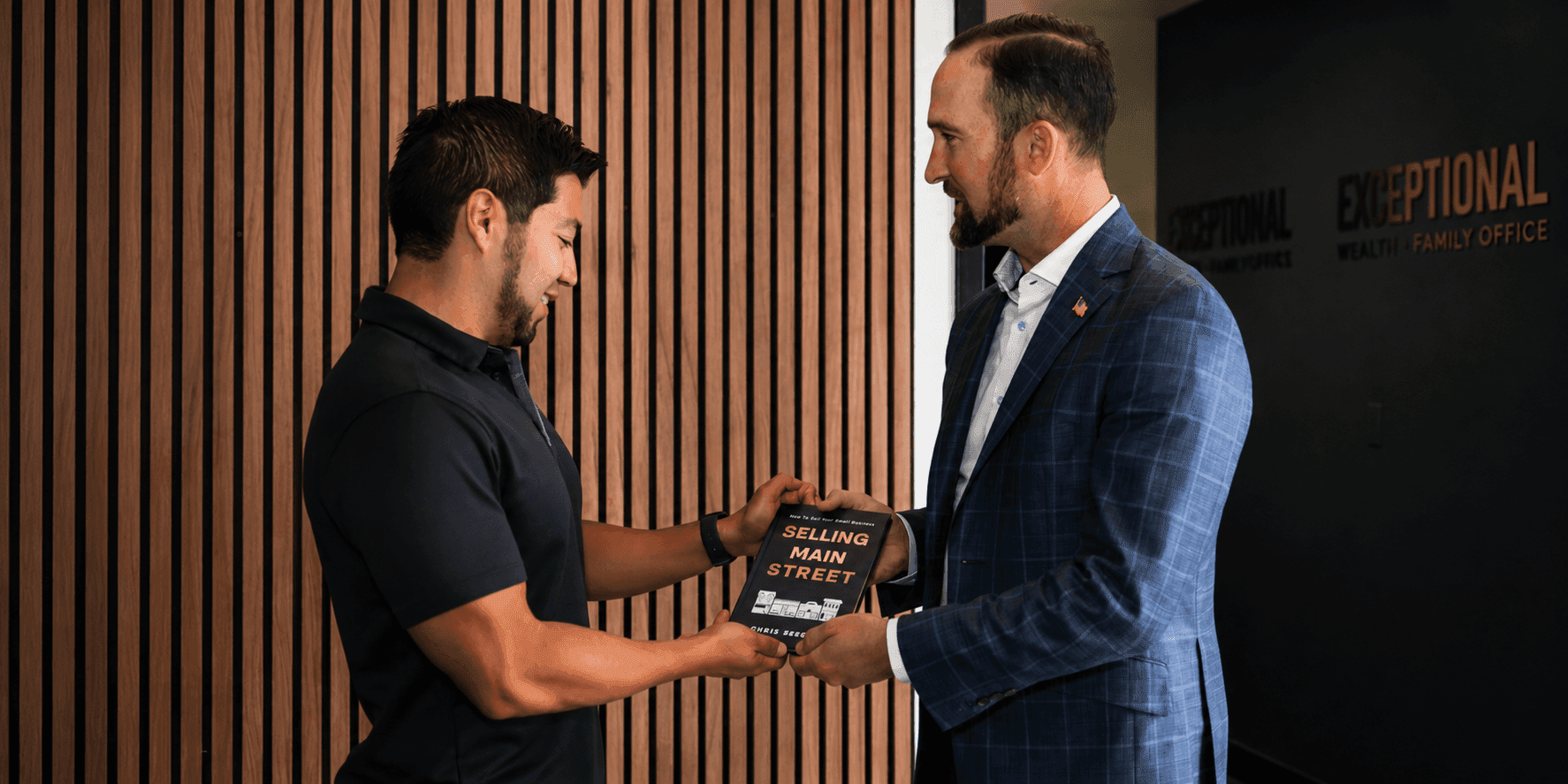 Chris Seegers hands a copy of Selling Main Street to a man inside an office.