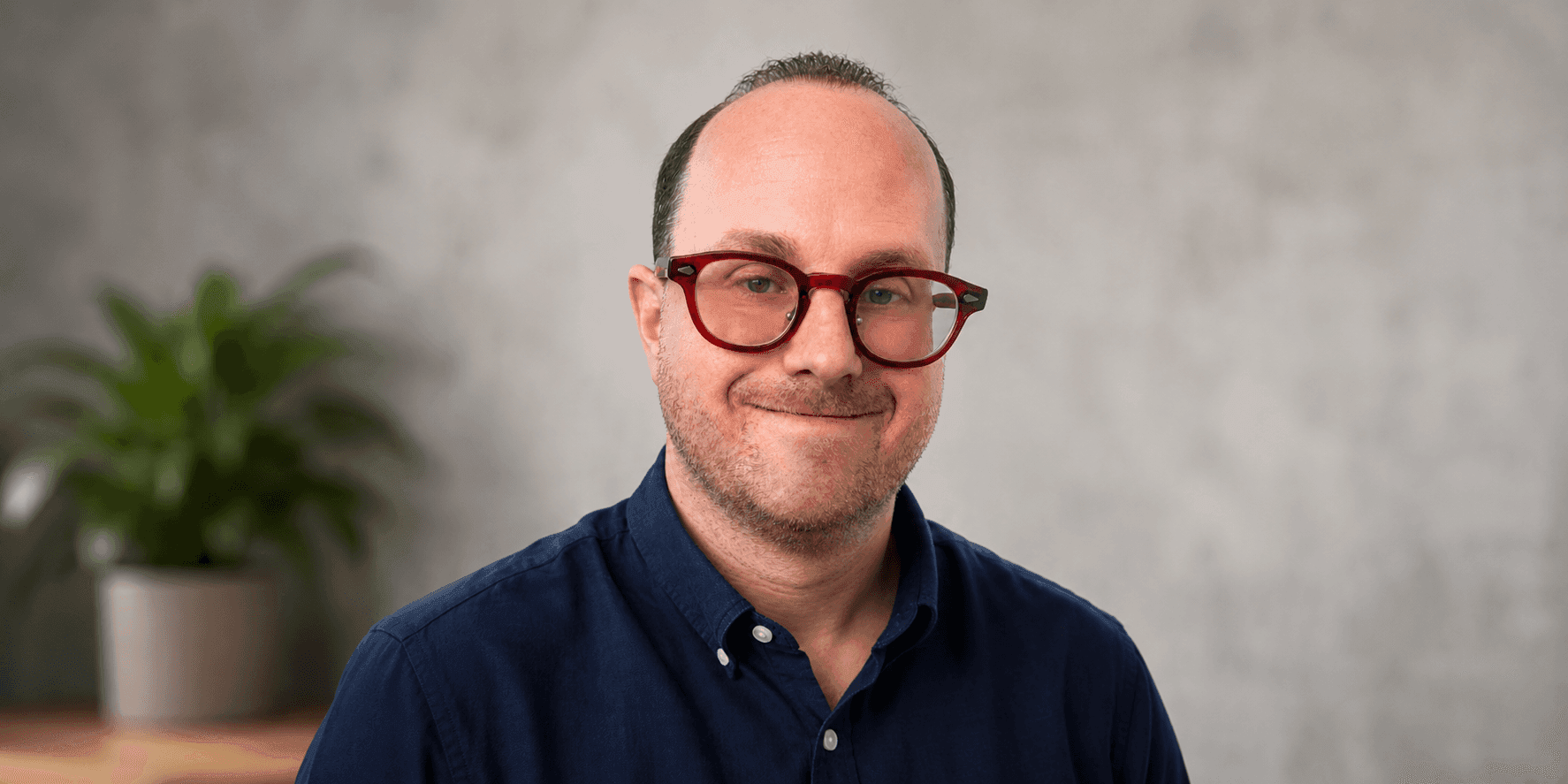 **Jonathan “Smilin J” Walker smiling in red glasses and navy shirt against a soft gray background.**