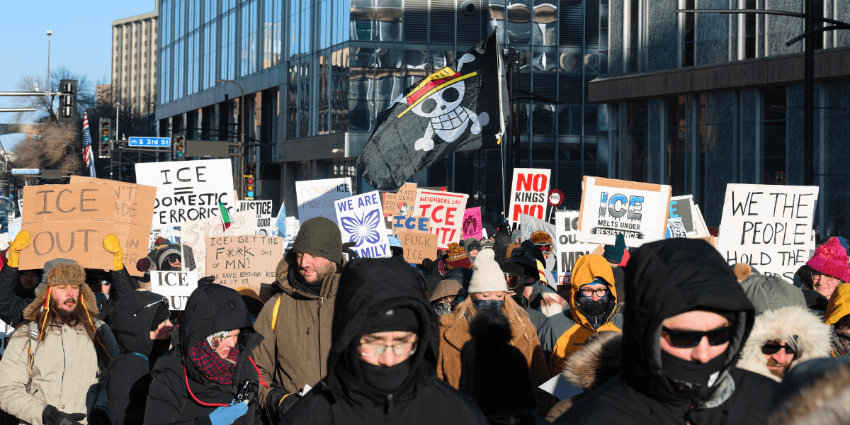 A diverse group of protesters holding signs and flags in the street, demonstrating against ICE and government policies on January 2026