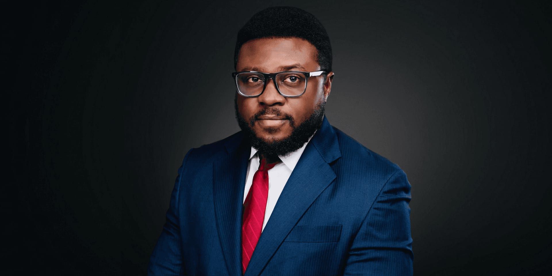 Professional portrait of Adewale Asimolowo in a navy suit, red tie, and glasses against a dark background.