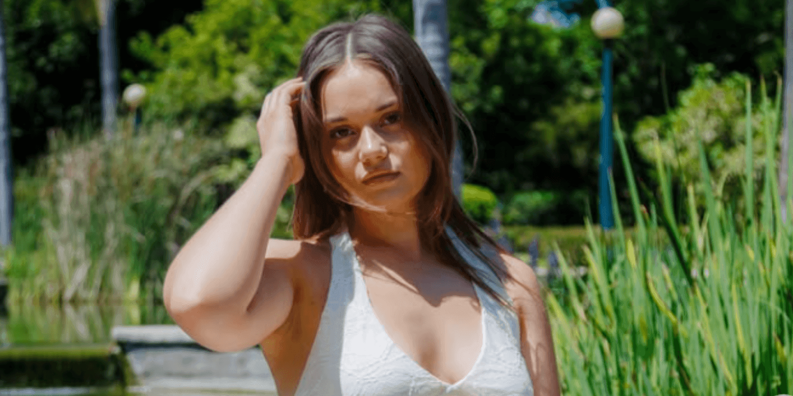 Jessi, a young woman with brown hair, stands outdoors in a white top, exuding authenticity and confidence."