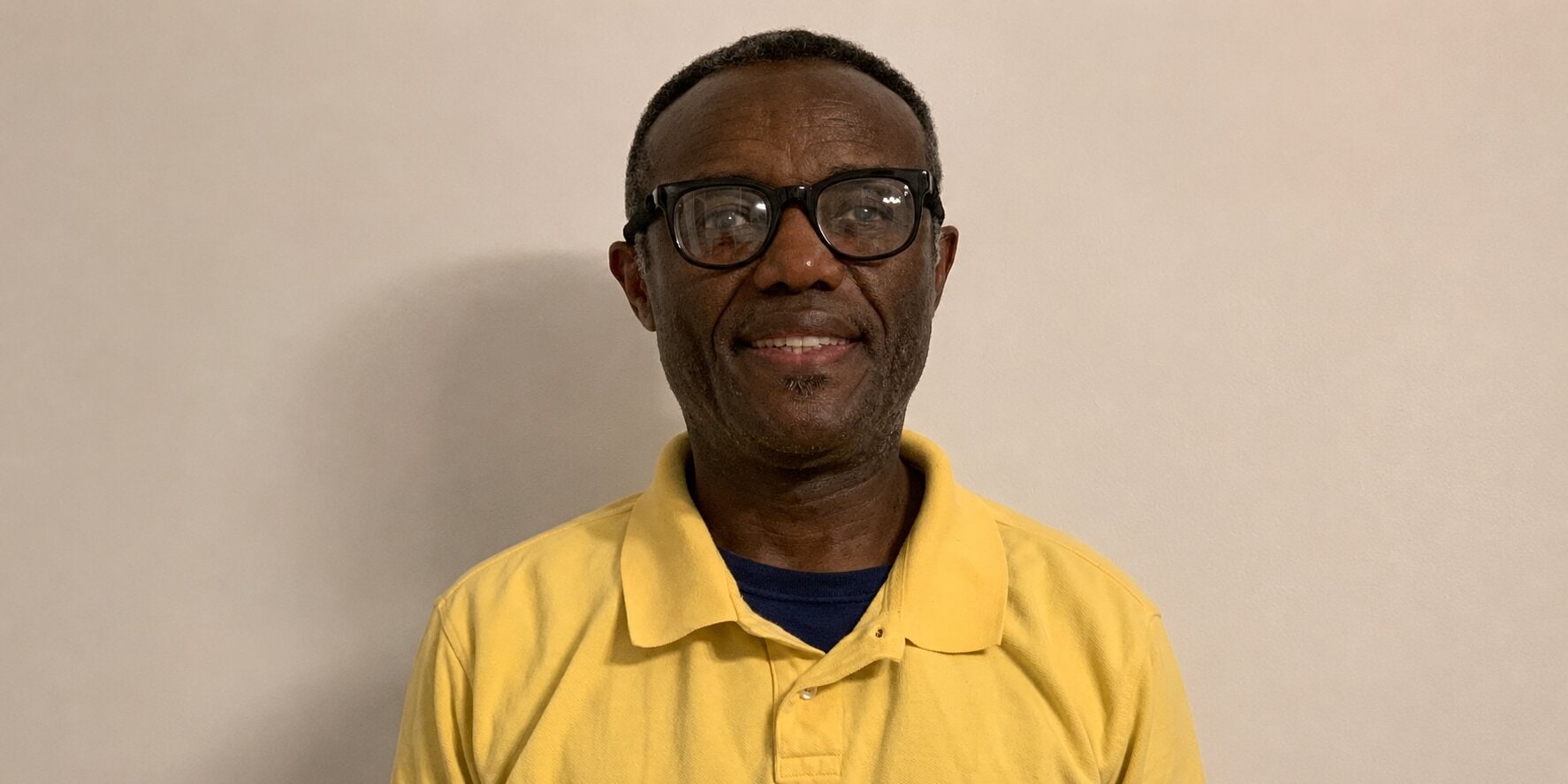 Charles Awusin Inko-Tariah wearing a yellow polo shirt and glasses, smiling against a plain background.