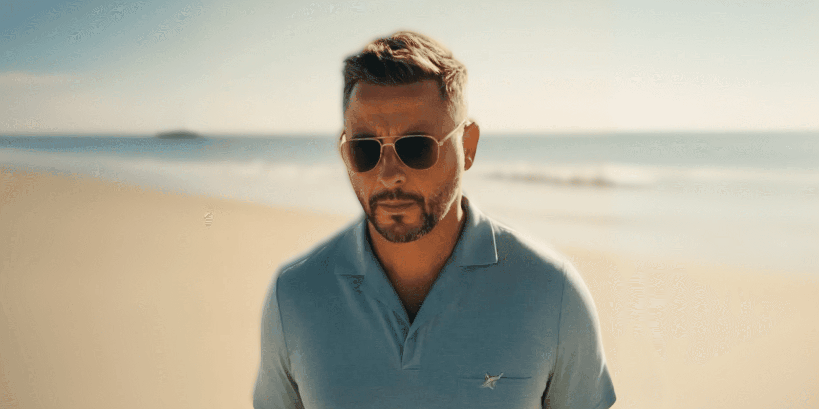 Man wearing sunglasses walking on a beach with a blurred ocean background