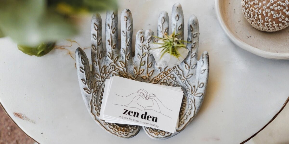 Zen Den business cards on decorative hand-shaped tray with flower on tabletop.