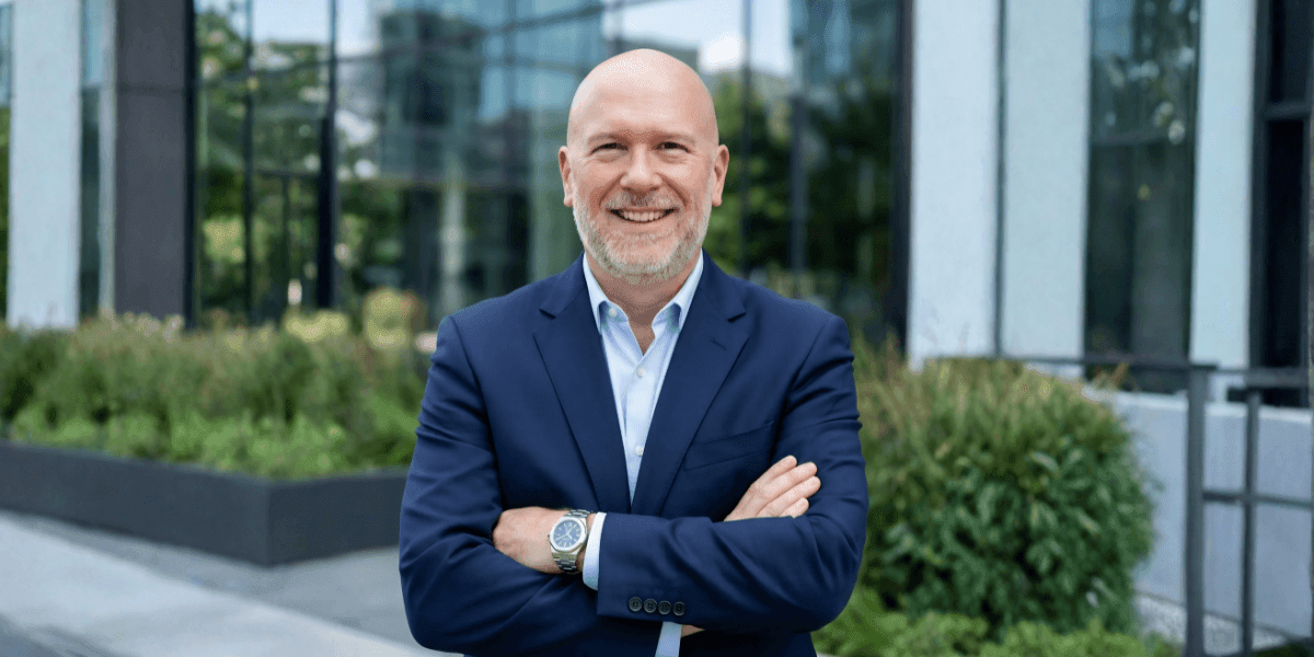 A bald man in a suit and tie stands confidently in front of a building, representing leadership in retirement planning.