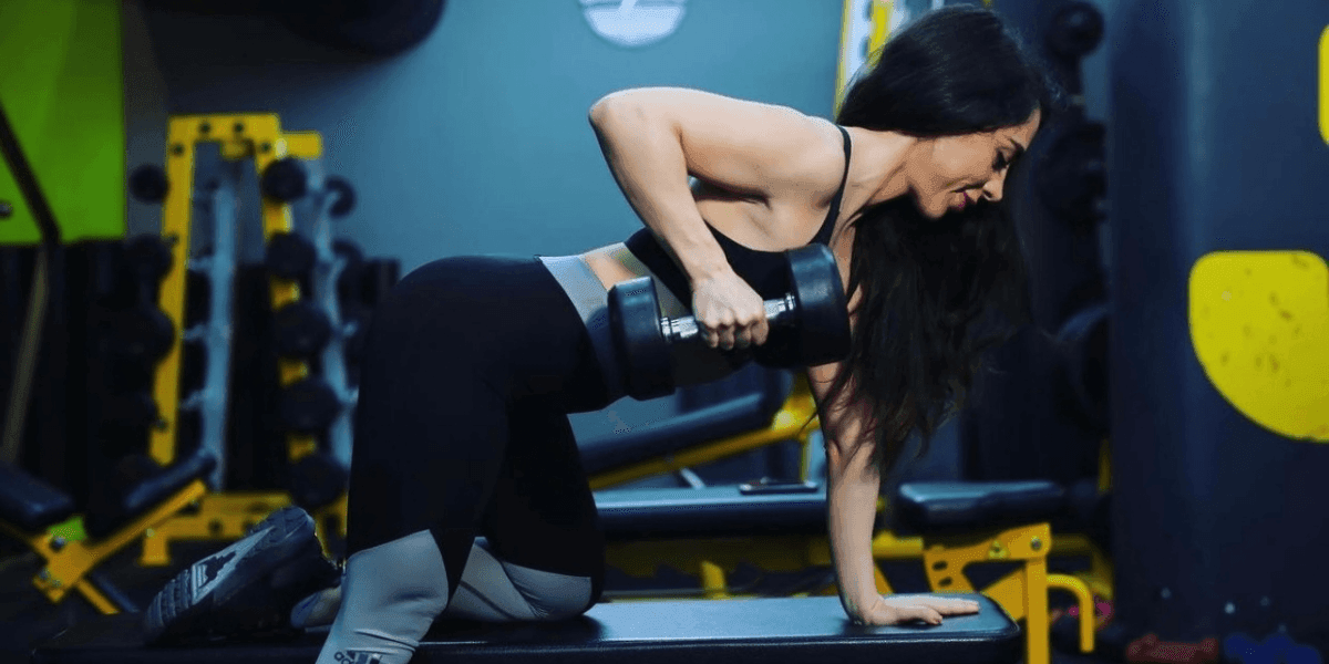 "Focused woman lifting dumbbells in the gym, wearing black and grey athletic wear, performing strength training exercises."