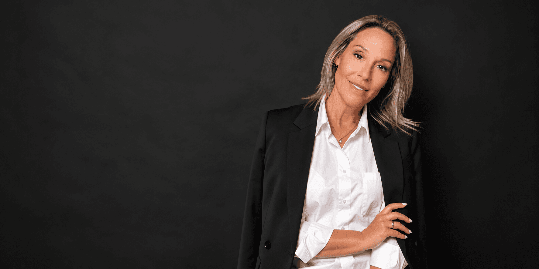 Coach Julianne wearing a white shirt and black blazer in a professional portrait against a black background.