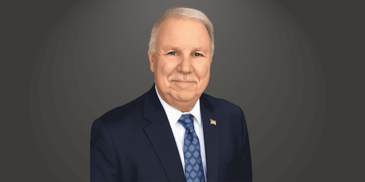 "Professional portrait of Mac McCall, a seasoned airport operations expert with a distinguished career in aviation leadership, wearing a suit and tie."