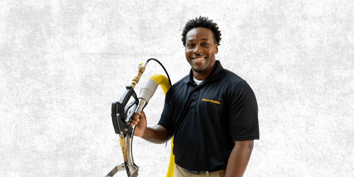Stanley Steemer technician holding professional cleaning equipment against a light background.
