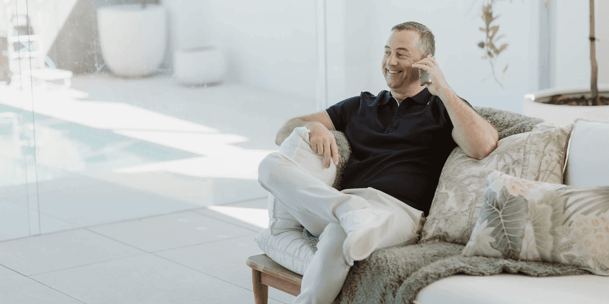 Jarrod Cooper ND sitting on a sofa in a bright room, smiling while talking on a mobile phone.