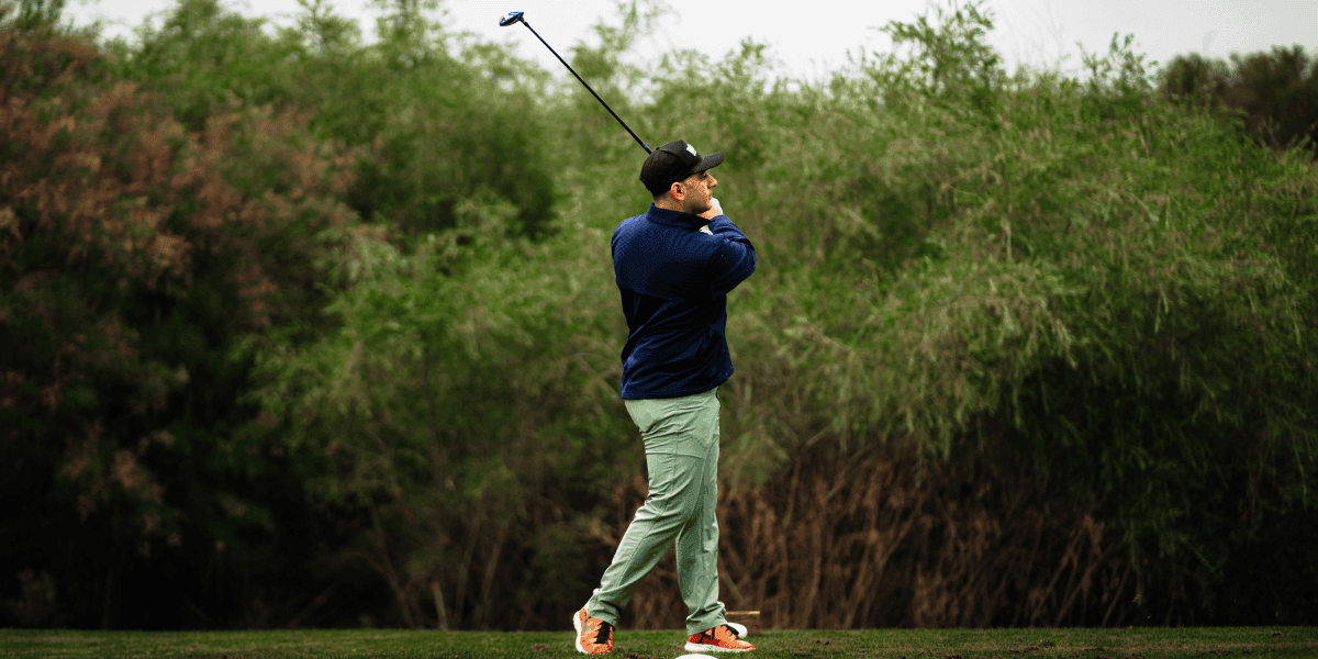 Image ALT Text Generator said: A person swings a golf club on a course surrounded by green foliage.