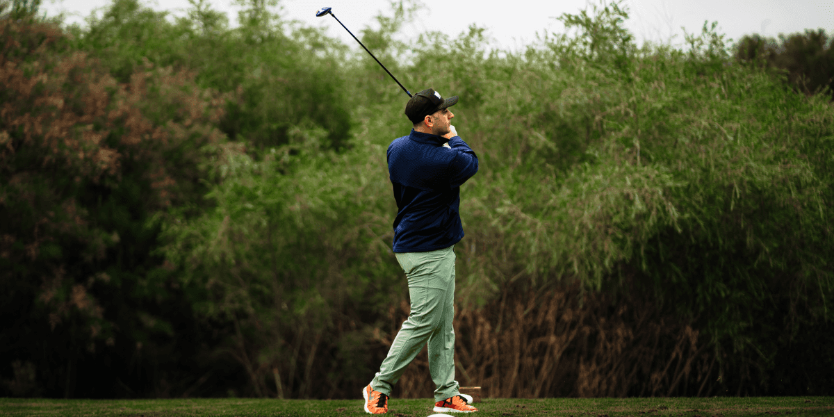Image ALT Text Generator said: A person swings a golf club on a course surrounded by green foliage.
