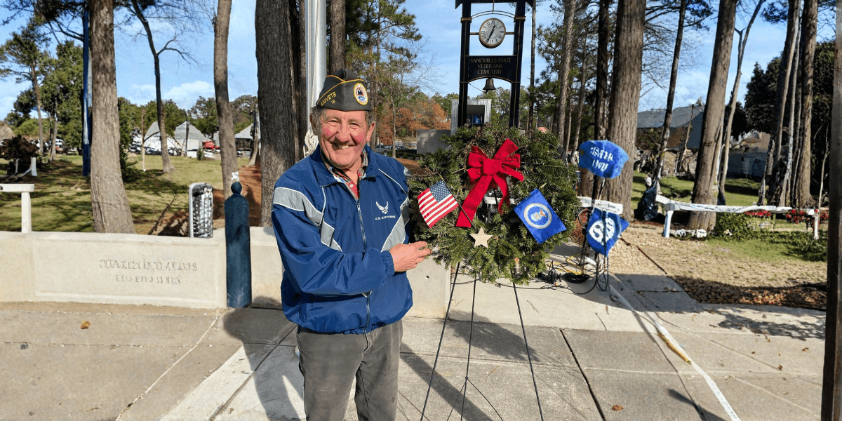 "David Hamel, a U.S. Air Force veteran, smiles while holding a wreath at a wreath-laying ceremony, honoring service."