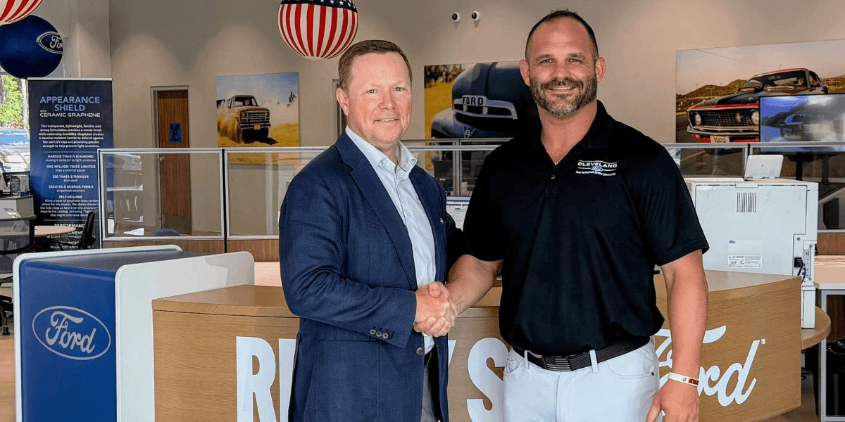 Anthony Boyd shakes hands with David Hudson inside a Ford dealership showroom.