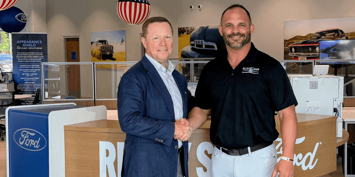 Anthony Boyd shakes hands with David Hudson inside a Ford dealership showroom.