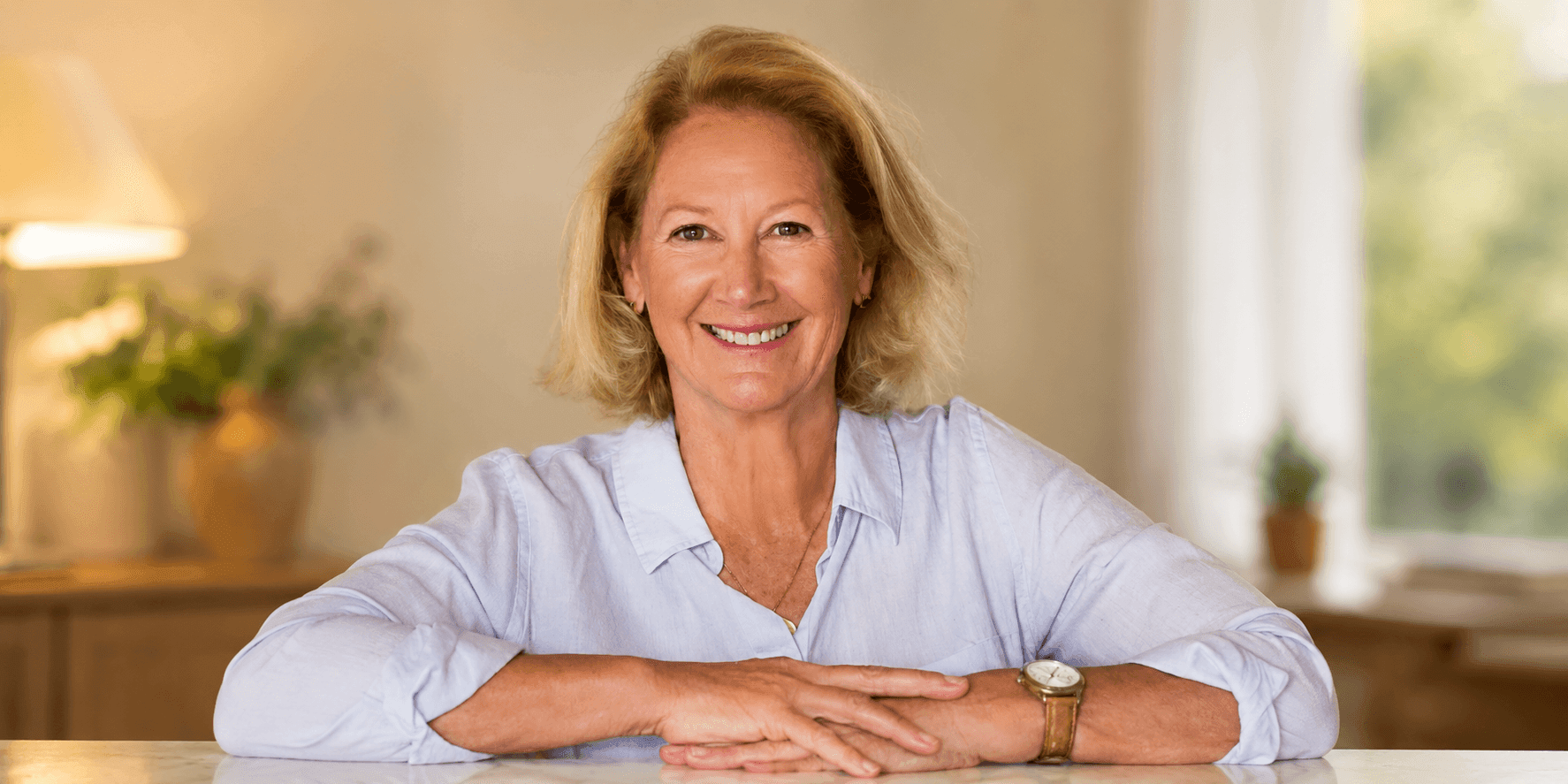 Christine Frisbee smiles at the camera while seated at a table, representing her strength and artistic spirit amid life's challenges.