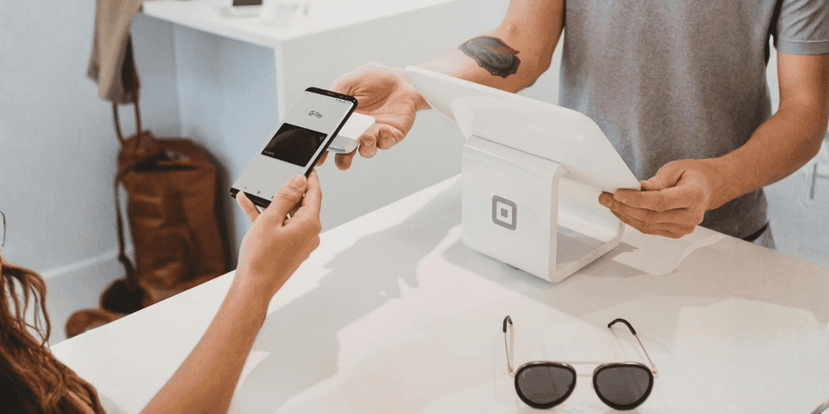 A person using Google Pay on their smartphone for a secure transaction at a point-of-sale terminal with Square.