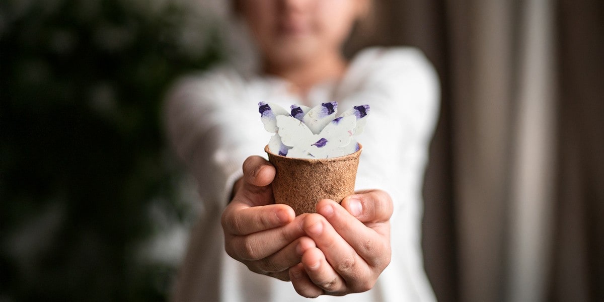 Close-up of a child holding a small flower pot filled with delicate butterfly-shaped flower tags made from pressed flowers, showcasing eco-friendly and handmade decorative tags.