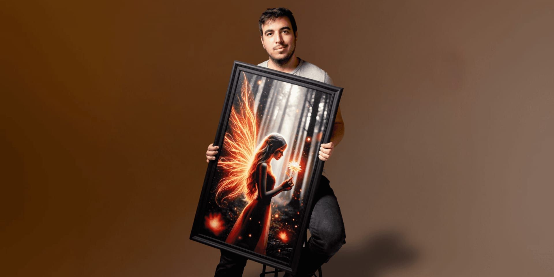 Man holding framed glowing fantasy fairy artwork with fiery wings against a studio background.