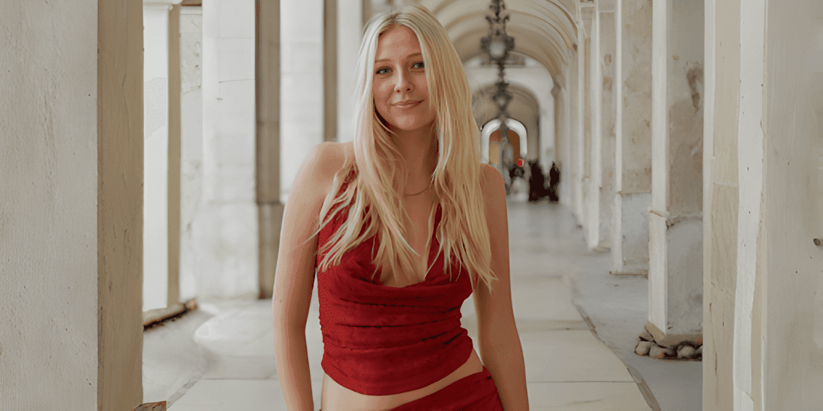 Young woman in a red outfit standing beneath an elegant stone archway, smiling at the camera.