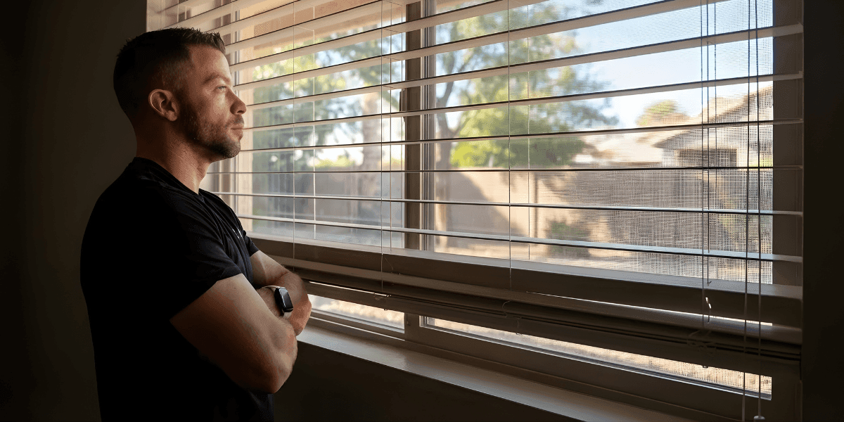 A man standing by a window, looking outside thoughtfully, reflecting on his emotional journey and trauma bond recovery.