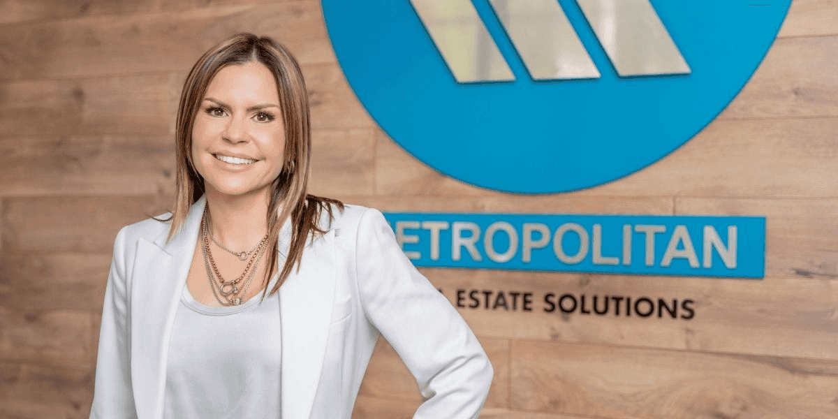 Alejandra Silva, founder of Metropolitan Real Estate Solutions, standing confidently in front of her company’s logo, smiling.
