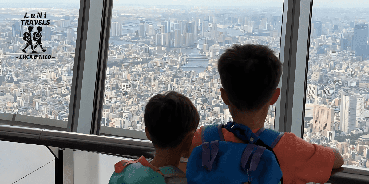 Two kids with backpacks admire the Tokyo skyline from a high observation deck.