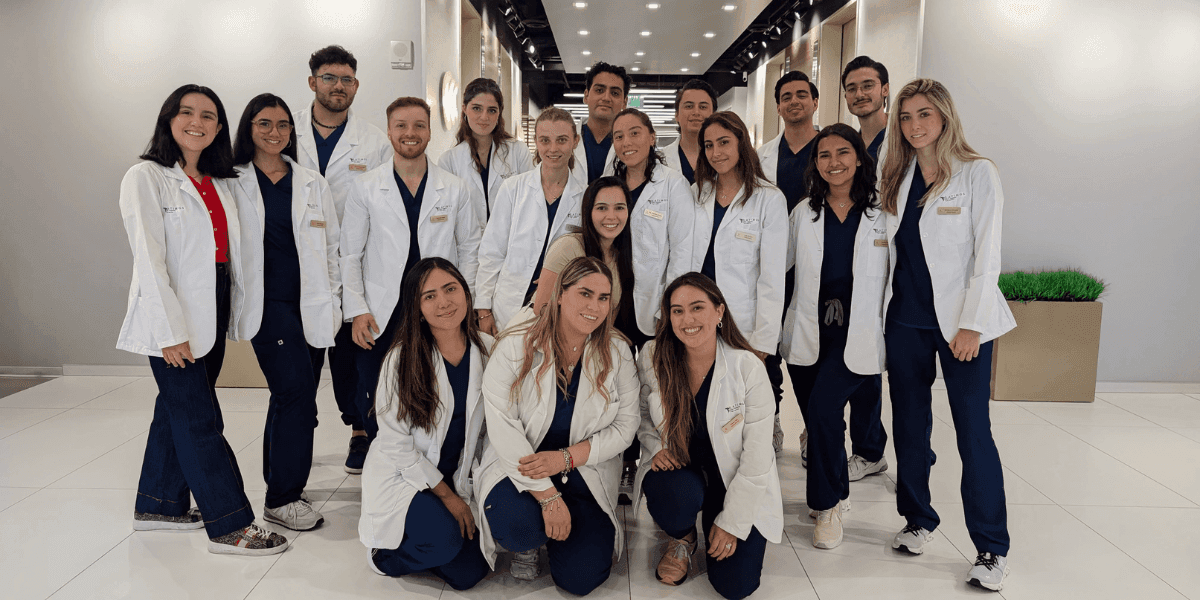 A diverse group of Latin American medical graduates in white coats, gathered for a photo in a modern setting.